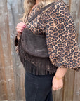 Person wearing a leopard print jacket holding a chocolate brown suede handbag with fringing on her shoulder