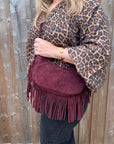 Person wearing a leopard print top and holding a burgundy suede crossbody bag with fringe detail