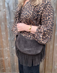 Person wearing a leopard print jacket holding a dark brown suedecrossbody bag with fringe detail