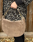 Person holding a taupe suede handbag with a leopard print coat s