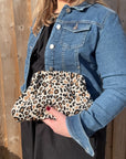 A person holding a leopard print knitted cloud bag with a hinged, snap closure.