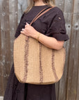 Woman wearing a brown dress holding a beige and brown raffia tote bag.