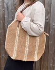 Woman wearing a white shirt, holding a large cream and beige raffia tote bag.