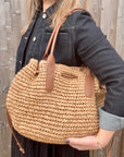 Woman wearing a black dress and denim jacket, holding a beige raffia shoulder handbag.