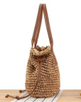 Woven straw bag with brown leather straps on a white background