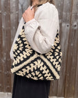Woman wearing a white shirt holding a black and cream raffia tote bag.