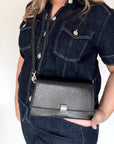 woman wearing a dark denim jacket with a black faux leather clutch/ crossbody handbag.