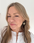 Woman wearing a white shirt with black and gold beaded disc earrings.