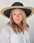 Woman wearing a black and beige straw hat against a plain background