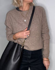 Woman wearing a beige sweater and black pants, holding a black bucket handbag.