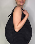 Woman wearing a black dress, holding a black woven handbag.
