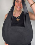 Woman wearing a black dress, holding a black woven handbag.