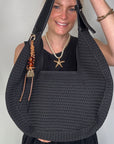 Woman wearing a black dress, holding a black woven handbag.