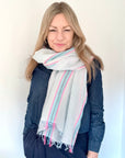 Woman wearing a light blue and pink scarf over a blue denim shirt.
