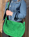 A woman wearing a denim jacket is holding a bright green large suede crossbody swing bag with a green-colored chain strap.