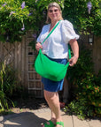 Woman holding a green bag outdoors with greenery in the background
