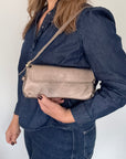 Woman wearing a denim jacket holding a bronze clutch handbag against a white background.