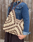 Woman wearing a denim jacket, holding a brown and cream raffia shoulder bag.