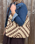 Woman wearing a denim jacket, holding a brown and cream raffia shoulder bag.