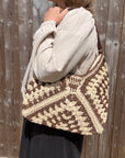 Woman wearing a white shirt, holding a brown and cream raffia shoulder bag.