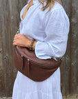 Woman wearing a white outfit holding a brown leather bag against a wooden fence.