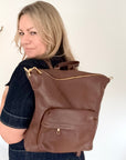 Woman wearing a brown leather backpack with gold accents and zippers