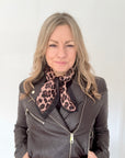 Woman wearing a grey leather jacket with a brown animal print square scarf.