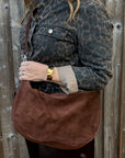 woman holding a brown crossbody bag against a wooden fence