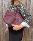 woman wearing a leopard print denim jacket holding a burgundy woven leather textured handbag.