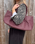 woman wearing a leopard print denim jacket holding a burgundy woven leather textured handbag.