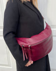 A person wearing a black coat is carrying a burgundy XL leather crossbody bag with silver hardware.