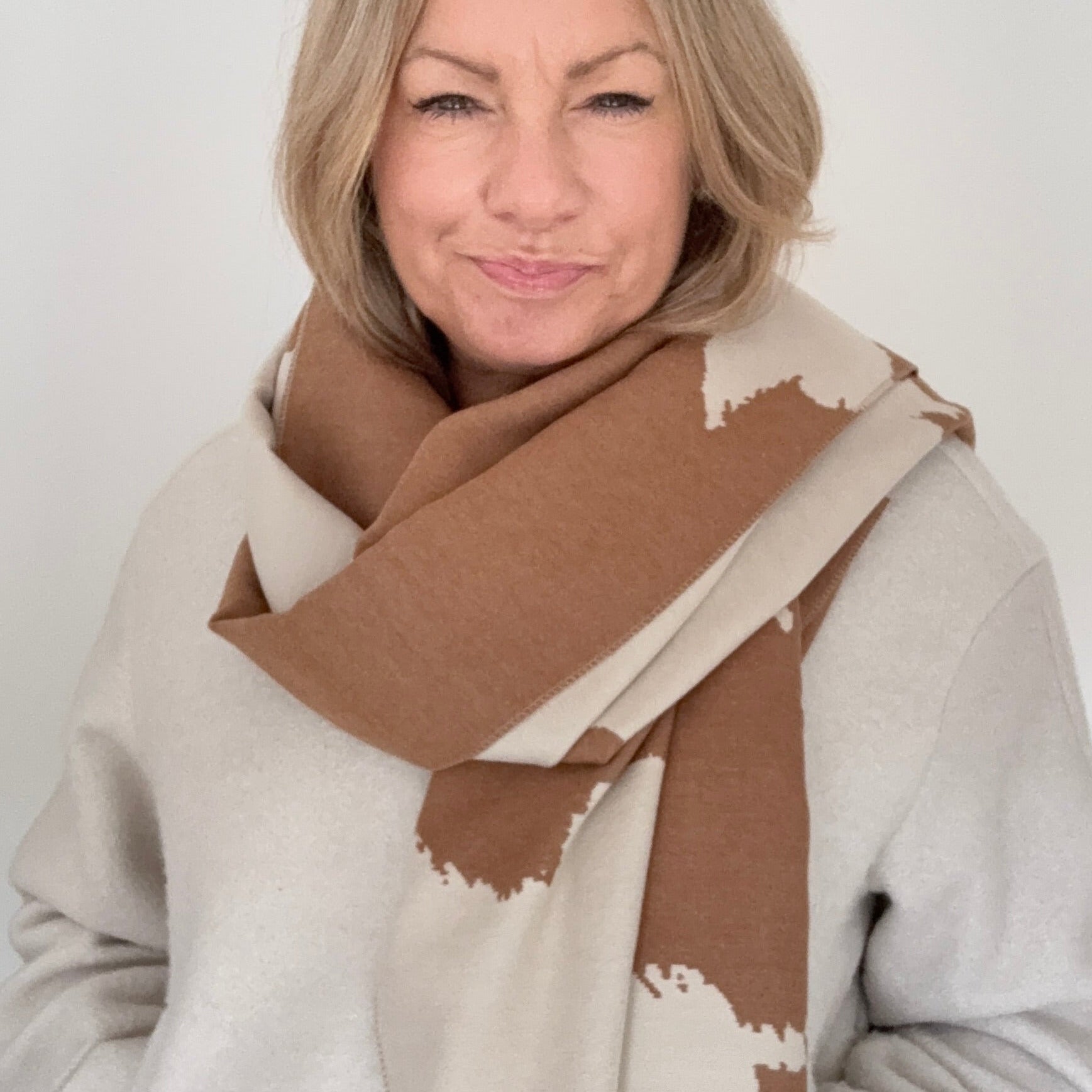 Woman wearing an Autumn Winter camel and cream cow print patterned blanket scarf for layering