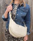 Woman wearing a denim jacket and leopard print dress holding a cream crossbody handbag.