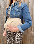 Woman wearing a denim jacket and leopard print skirt holding a cream knitted cloud bag.
