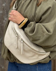 Woman wearing a green shirt with a large cream crossbody bum bag.