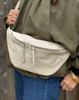 Woman wearing a green shirt with a large cream crossbody bag with a wooden background.
