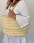 woman holding a beige woven tote bag against a plain background