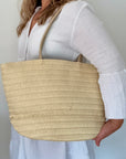 woman holding a beige woven tote bag against a plain background