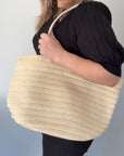 A person holding a cream-colored raffia tote bag with a PU handle strap.