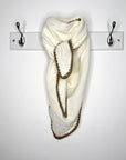 cream and taupe knitted scarf draped over a silver hook on a white wall.