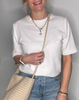 Woman wearing a white shirt and wearing a cream woven crossbody handbag.