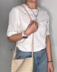 Woman wearing a white shirt and wearing a cream woven crossbody handbag.