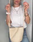 Woman wearing a white shirt and wearing a cream woven crossbody handbag.