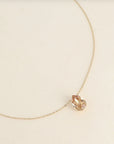 Gold necklace with a teardrop-shaped pendant on a beige background