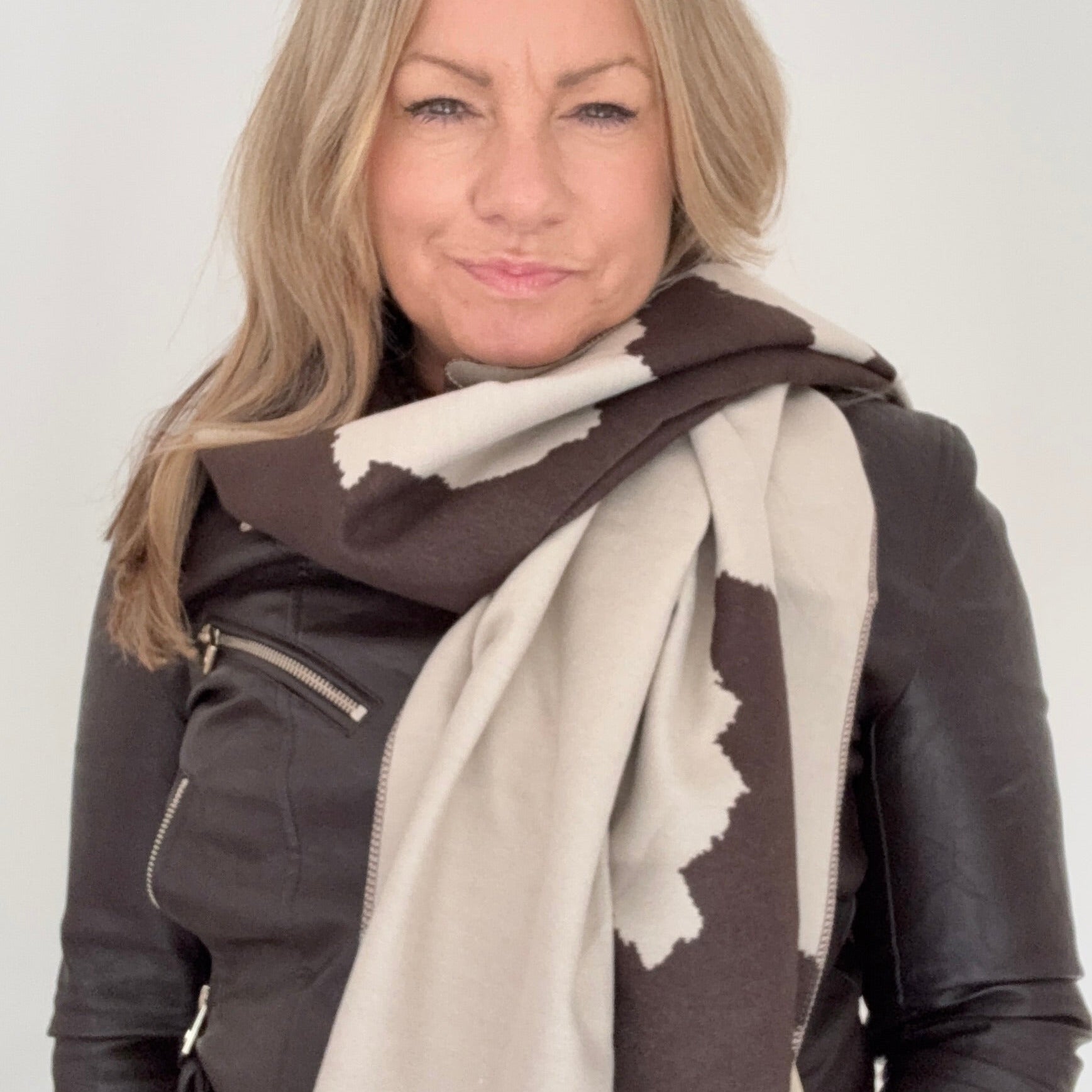 Woman wearing a brown leather jacket and a large scarf with a  Dark Brown & Cream Cow print pattern for Autumn Winter