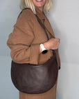 Woman holding a dark brown leather crossbody/ shoulder bag