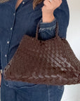 woman holding a brown woven handbag against a white background