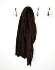 Brown knitted scarf hanging on a hook against a white wall