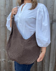 Woman wearing a white shirt and holding a brown woven crossbody handbag.