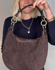 Woman holding a dark brown suede crossbody/ shoulder handbag
